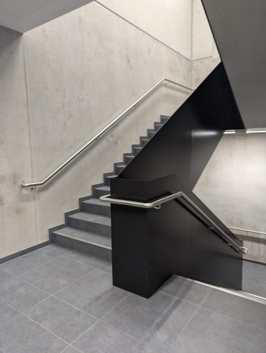 Treppenhaus mit grauen Wänden und einer modernen, schwarzen Treppe.