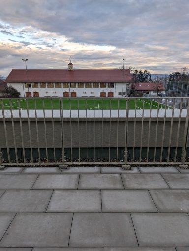 Blick auf ein Stadion mit Rasenfläche und einem Gebäude im Hintergrund.