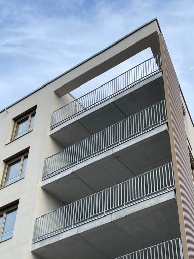 Moderner Wohnblock mit Balkonen und einem klaren blauen Himmel im Hintergrund.