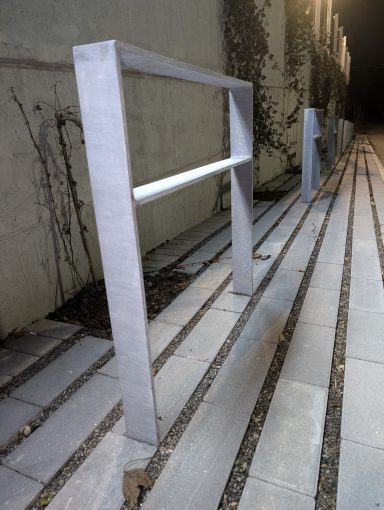 Graue Metallstützen zum Abstützen an einer Treppe, umgeben von Pflastersteinen.